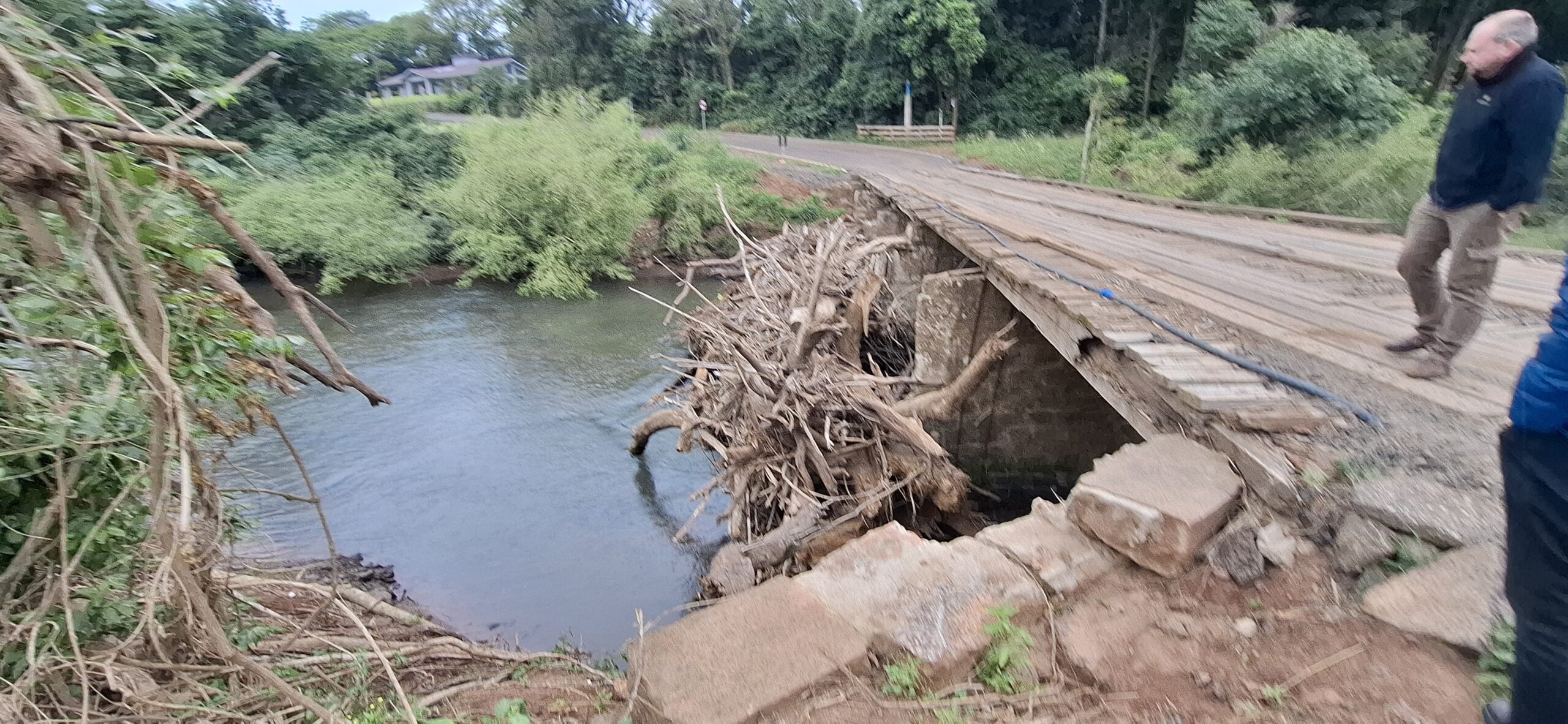 Obstrução por galhos e detritos acumulados junto a uma ponte de madeira